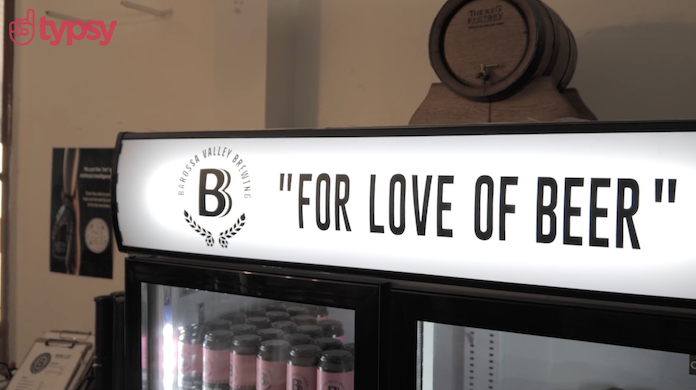 The upper half of a glass-fronted beer fridge with the words For the Love of Beer across the top. The red Typsy logo is in the upper left hand corner of the image
